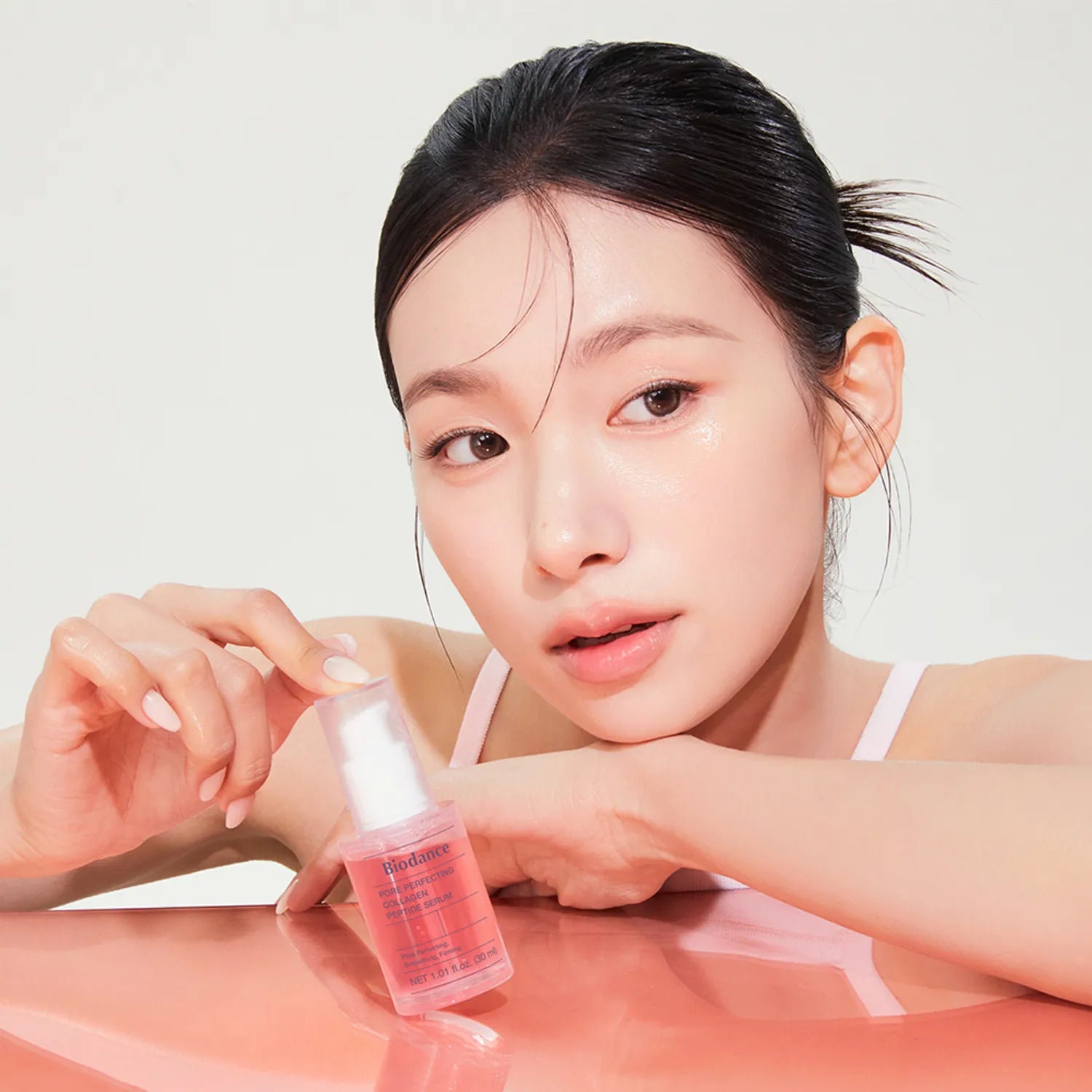 Woman holding a pink bottle with a white cap on a light background