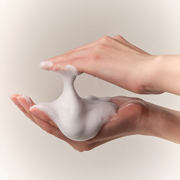 Two hands holding a small amount of white foam against a neutral background